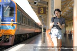 A woman wearing headphones listening to music from an app on a tablet while waiting for train 56KvP4