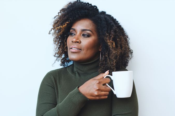 Black woman holding a cup of coffee and thinking