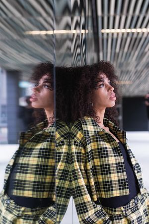 Stylish Black woman reflecting on glass wall in town