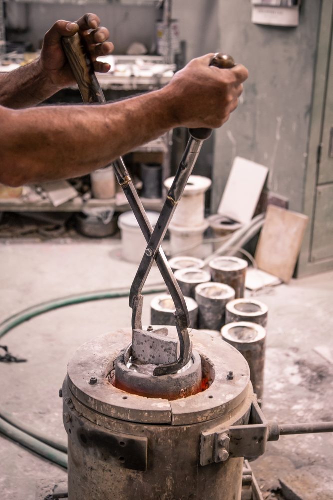 Man with lifting tongs taking metal ware from crucible