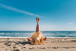 Woman in big hat lying on sandy beach