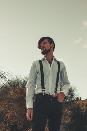 Man wearing dress shirt and straps standing outdoor and looking away