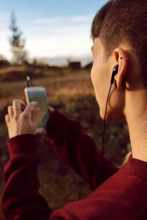 Young woman with piercing listening music on smartphone on hill