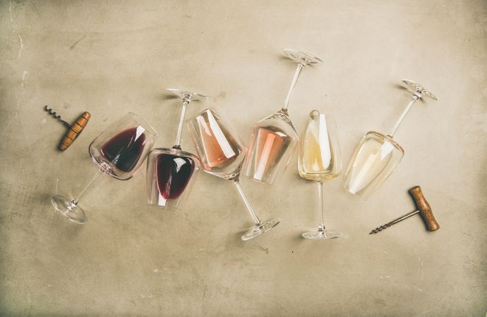 Glasses of wine laying on grey background with corkscrew