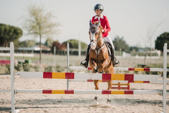 Teen girl riding horse and jumping over bars