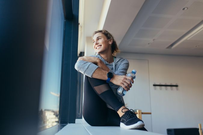 Smiling fitness woman holding water bottle sitting in a pilates gym
