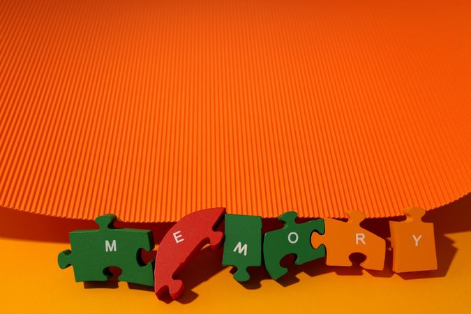 Orange duotone paper flat lay with puzzle pieces spelling out the word “Memory”