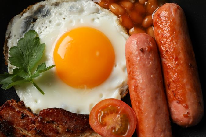 Top view of eggs, sausages and tomatoes on dark plate