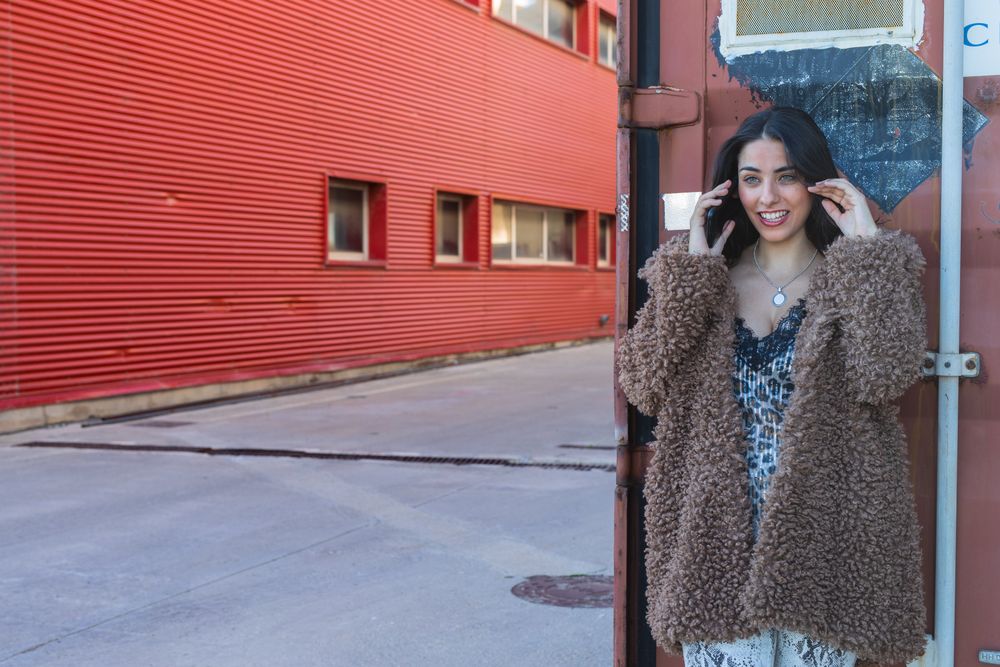 Trendy woman with smartphone near wall