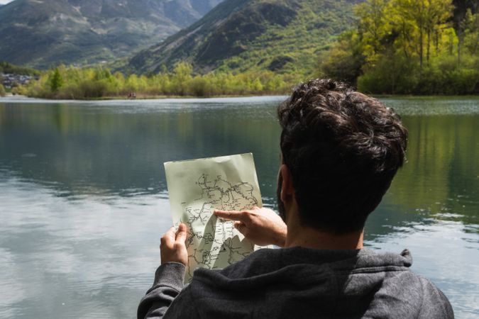 Traveling man reading map near lake in highlands