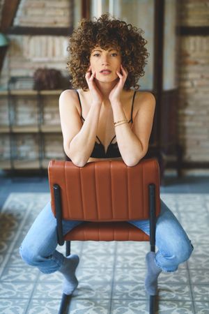 Woman with curly hair sitting on chair reversed looking at camera