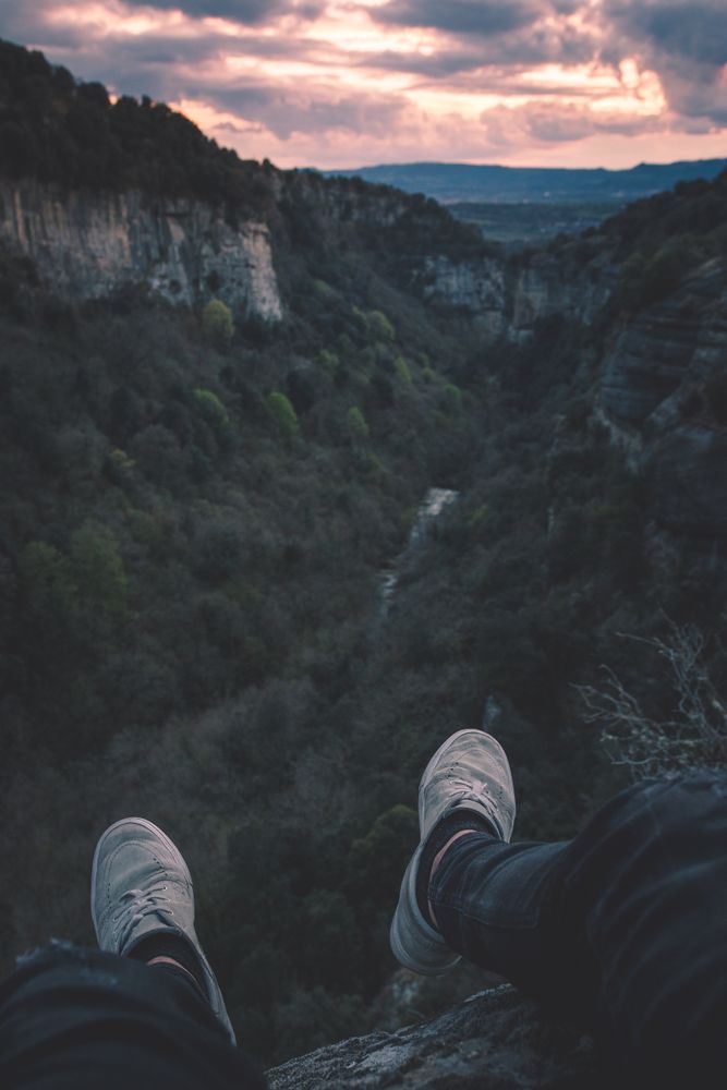 View to small river in canyon and legs of person sitting on the edge