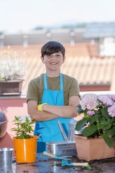 Young smiling teenager wearing gardening apron while standing on patio