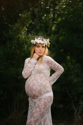 Pregnant woman with closed eyes in white lace dress touching chin while standing in forest