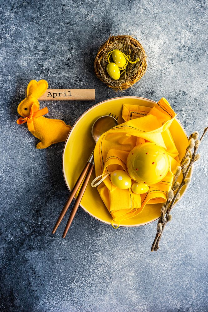 Top view of Easter table setting with yellow egg ornaments in yellow bowl