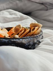 Side view of breakfast bowl of fresh orange slices, nuts and mini pancakes in morning light