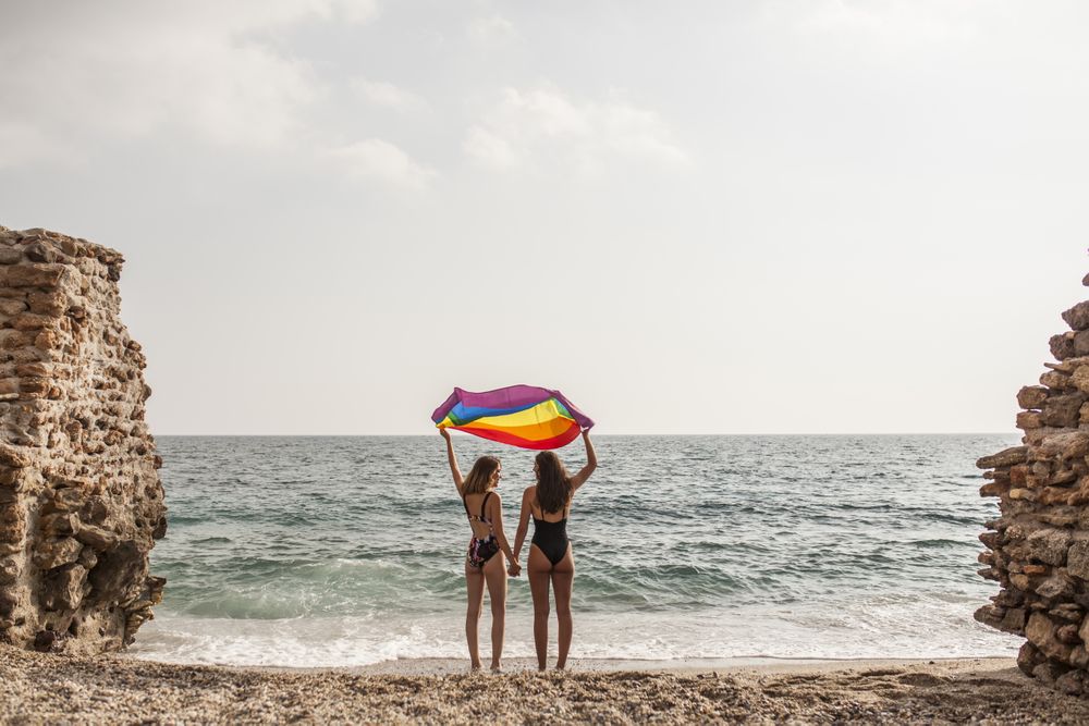 Females standing with rainbow flag on seashore