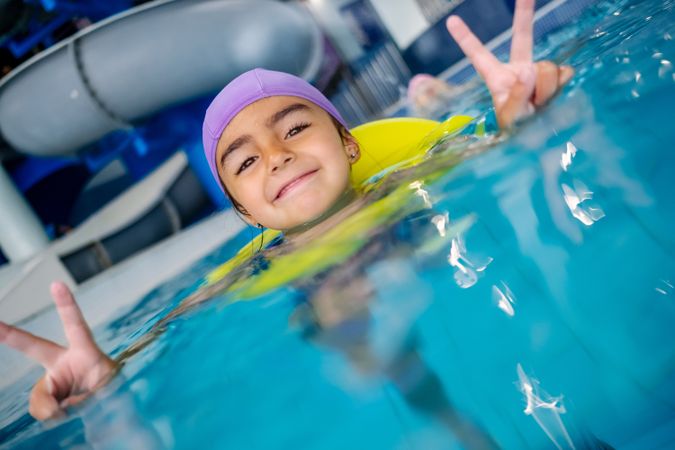 Happy girl gesturing V sign in swimming pool