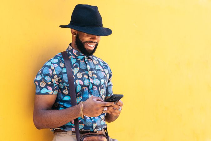 Stylish Black man using smartphone outdoors over yellow background
