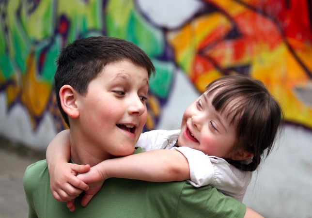 Boy playing with his sister with Down syndrome on his back