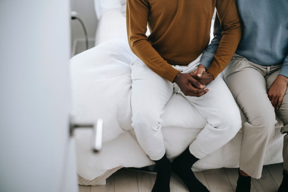 Cropped image of two Black men holding hands sitting on bed
