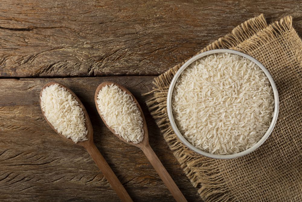 Rice in a ceramic bowl on brown wooden background.