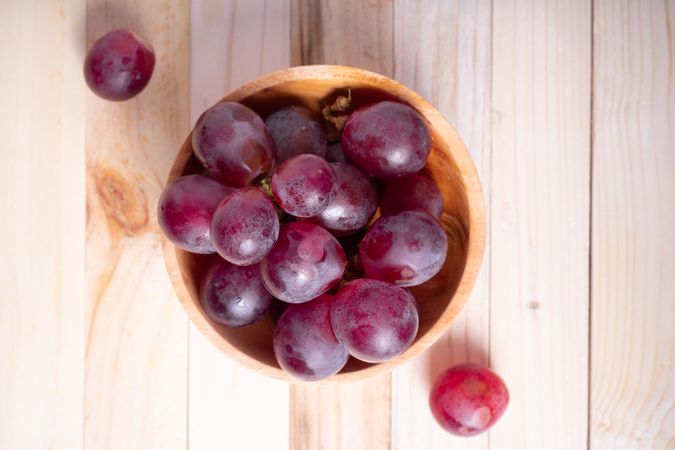 A bowl of red grapes sits on a wooden table