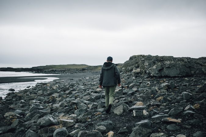 Back of man walking on rocky beach on overcast day