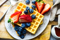 Top view of waffle breakfast with blueberries & strawberries served with syrup on the side