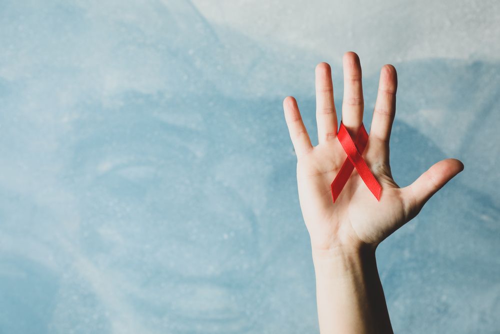 Hand and red awareness ribbon against blue background, space for text