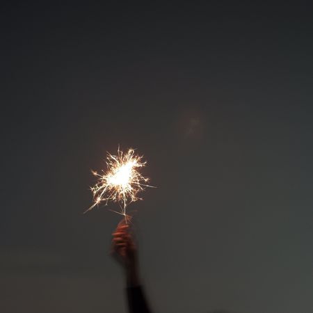 Blurry photo of person holding lighted sparkler during night time