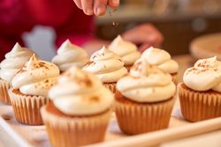 Faceless confectioner decorating cupcakes placed on white plate