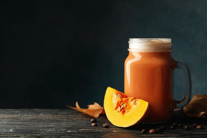Glass jar of pumpkin latte, coffee seeds and leaves on wooden background