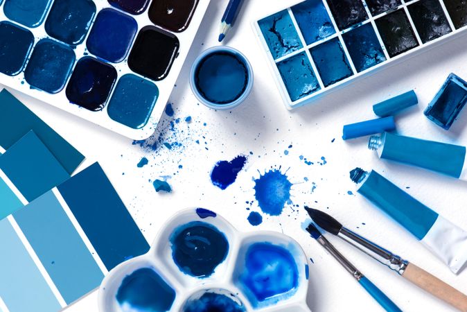 Blue paint splattered with palette and tubes on bright background