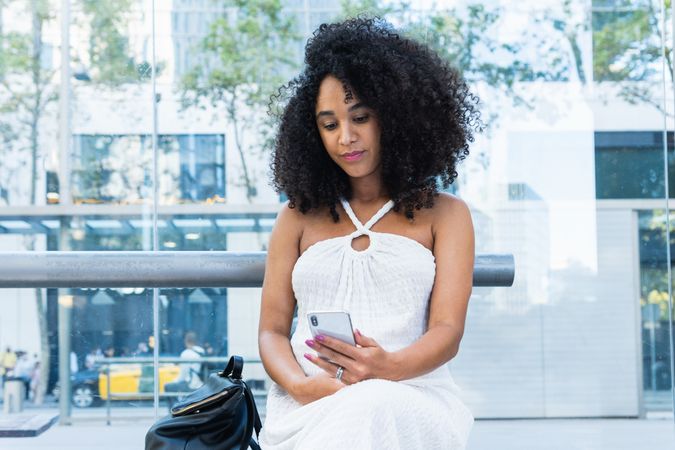Pregnant Black woman using smartphone on public transport stop