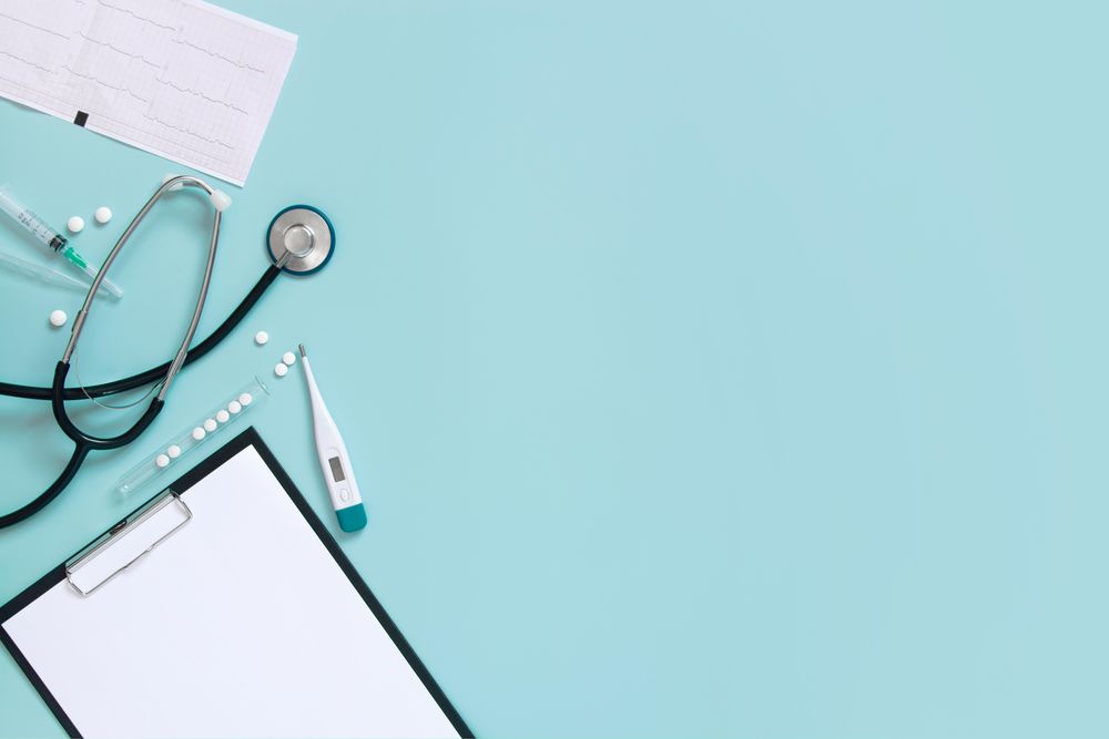 Top view of blue desk with doctor’s equipment and notepad, with copy space