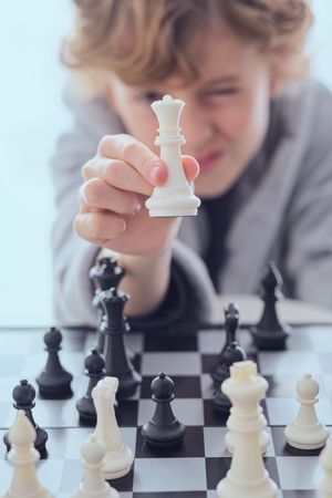 Preteen boy squinting and showing chess of piece queen