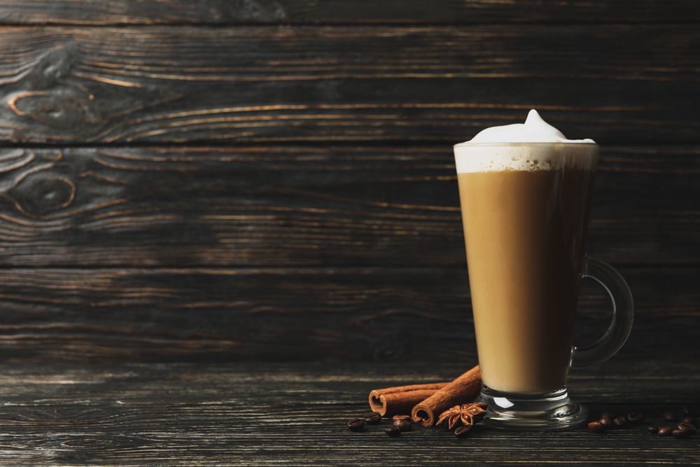 Glass cup of latte, coffee seeds and cinnamon on wooden background