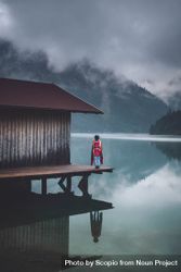 Person standing beside house on dock over lake under cloudy sky 5RBaJ5