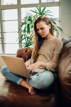 Young woman sitting on her couch working on laptop