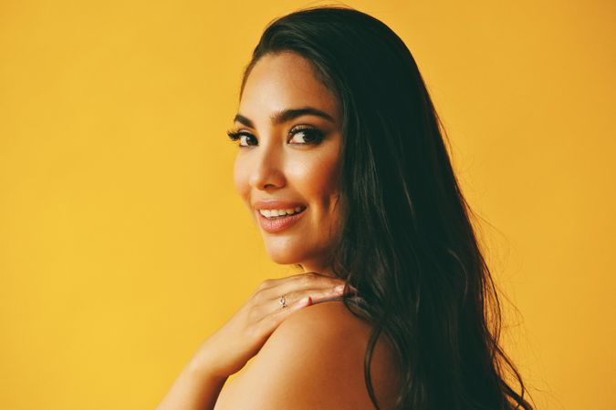 Hispanic woman looking around at camera in yellow room with her hand on her shoulder