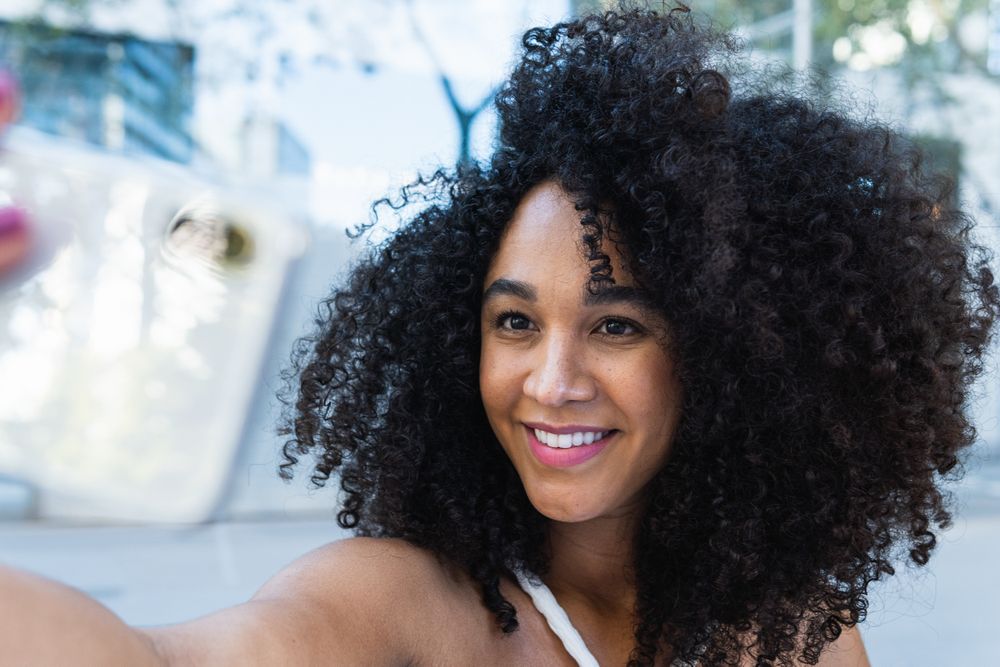 Happy Black woman with curly hair reaching hand to camera
