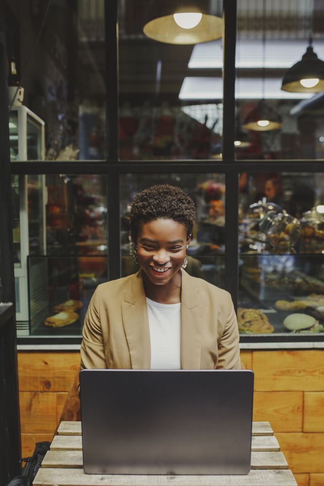Smiling Black woman sitting at table with laptop in cafe