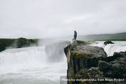 Man on cliff over waterfall, landscape bYRQY0