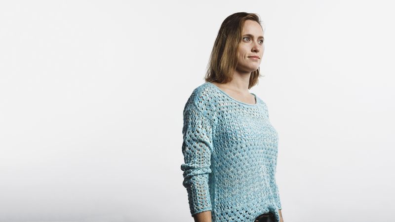 Side view of a woman in wool top standing against neutral background