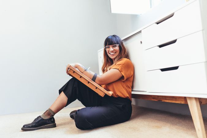 Female illustrator making a drawing sitting on floor in her office smiling and looking at camera