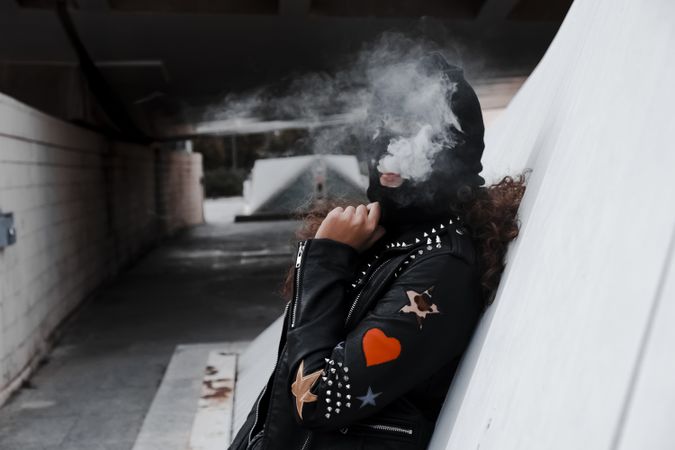 Woman in mask and jacket smoking on street