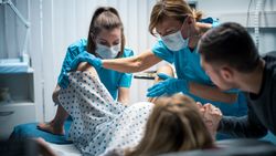 In the Hospital Woman in Labor Pushes to Give Birth, Obstetricians Assisting, Husband Holds Her Hand