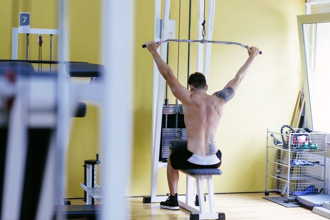 Tattooed male exercising his arms on pull down machine