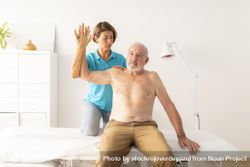 A female physiotherapist performs a massage and checks the mobility of the arm and shoulder of her mature patient 0v336G